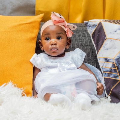 Cute baby girl sitting among vibrant cushions, showcasing innocence and cuteness.